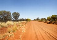 Remote red dirt road stretching into the horizon through dry bushland in the Australian Outback. Dirt road leading to Owen Springs Reserve