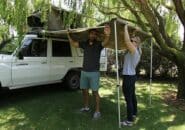 Travellers setting up a 4WD vehicle awning at a shaded grassy campsite in the Kimberley.