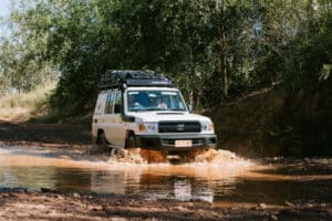 4WD tour vehicle driving through a muddy creek crossing in the remote Kimberley region.