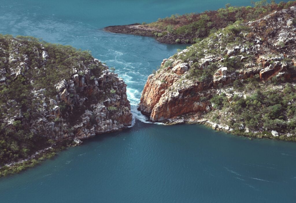 Aerial view of the Horizontal Falls in the Kimberley region, where turquoise tidal waters surge through narrow coastal gorges between rugged cliffs.