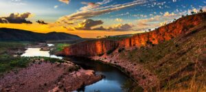 Kimberley river gorge at sunset with glowing red cliffs, winding waterway and dramatic sky, viewed from a high vantage point in Western Australia