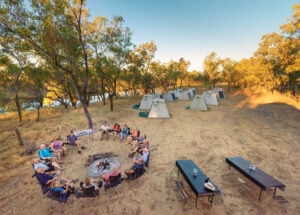 Exclusive Camp by a Billabong Kimberley Tours Travellers relaxing around a campfire beside a billabong with individual safari tents set up in the Kimberley bush. - Credit Meike Boynton Photography