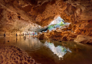 Hiking through Tunnel Creek Kimberley Tours - Group walking barefoot through shallow water inside the ancient limestone caverns of Tunnel Creek. Credit Meike Boynton Photography